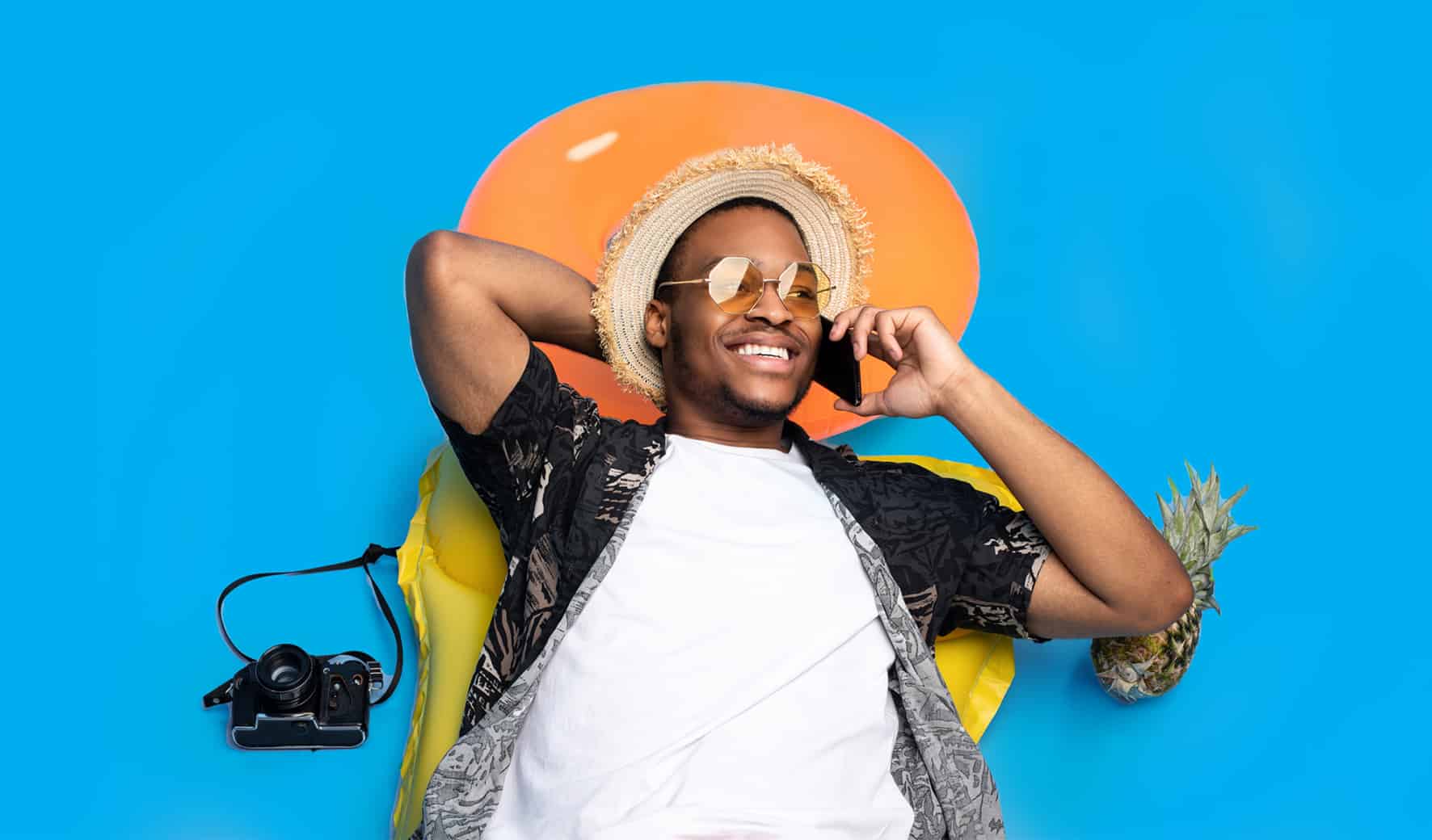 Lachende man met strohoed en zonnebril belt op vakantie, met ananas, camera en oranje zwemband op blauwe achtergrond