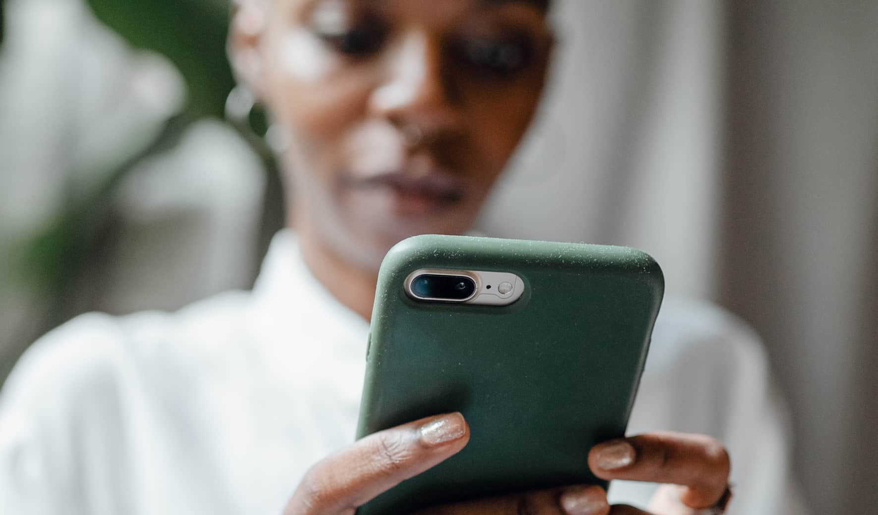 Vrouw bekijkt de achterkant van haar iPhone met groen hoesje terwijl ze Face ID probeert te gebruiken