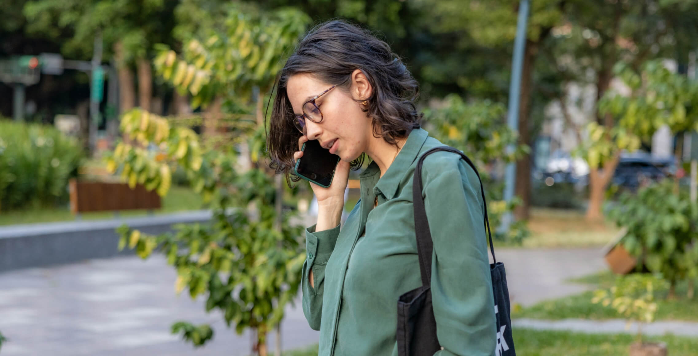 Vrouw met bril belt op haar smartphone terwijl ze buiten loopt, telefoonnummer zoeken